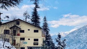 A two-story building with a balcony, surrounded by snow-covered trees and mountains in the background.
