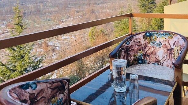 A balcony with a table and chairs, overlooking a mountainous landscape with a village below.