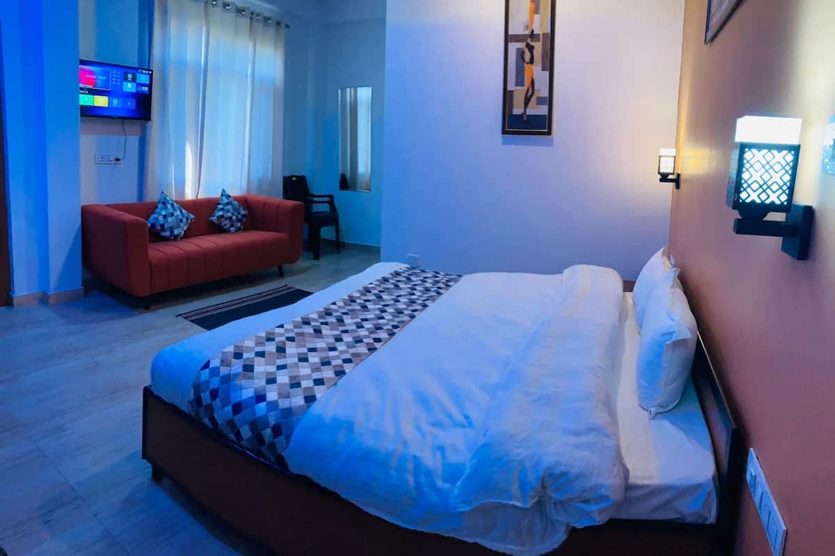 A hotel room with a bed, a red sofa, a TV, and a wall-mounted light fixture.