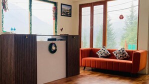 A reception area with a wooden desk, a red sofa with patterned cushions, and a view of mountains through large windows.