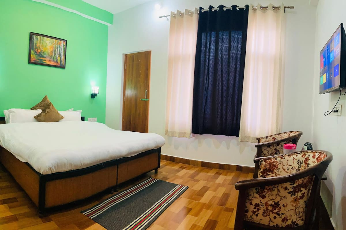 A hotel room with a bed, a chair, a painting on the wall, and a window with curtains.