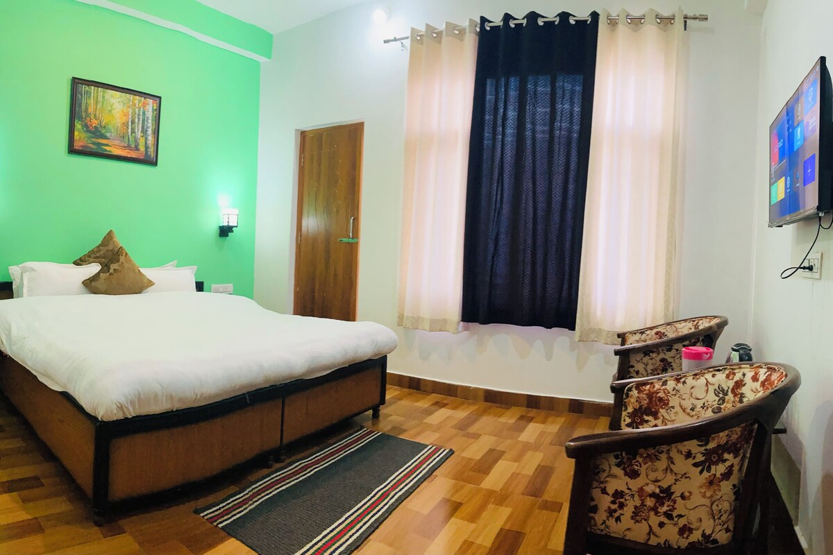 A room with a bed, a chair, a painting, a window with curtains, and a television.