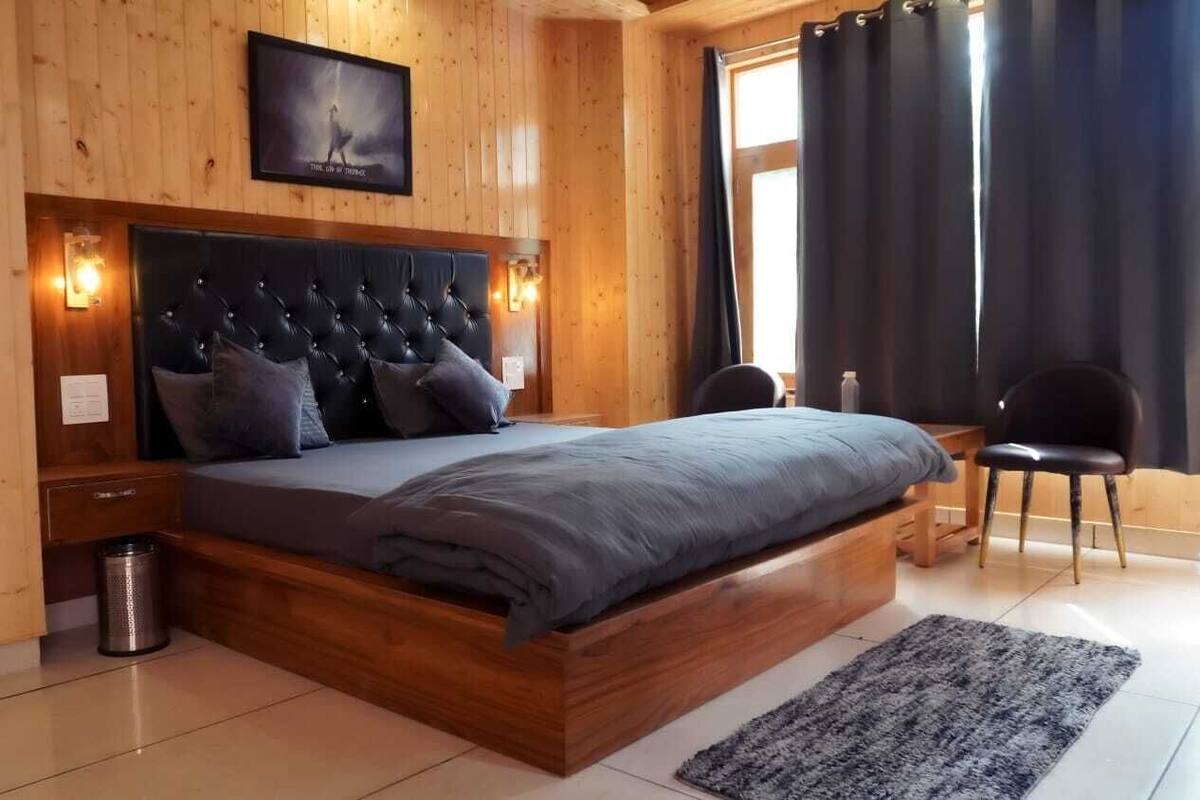 A wooden-paneled room with a large bed, a headboard, a small table, a chair, and a picture on the wall.