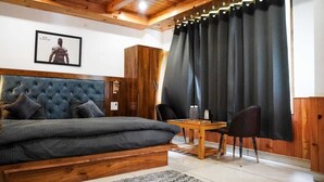 A bedroom with a large bed, a wooden headboard, a small table with chairs, and a dark curtain. - Odin Hostel Kasol (Bhuntar)