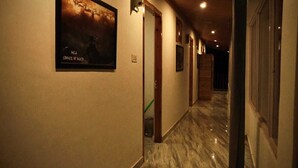 A hallway with a marble floor, framed artwork on the walls, and wooden doors. - Odin Hostel Kasol (Bhuntar)