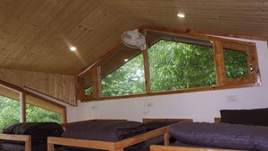 A room with wooden bunk beds, a ceiling fan, and large windows with a view of greenery. - Odin Hostel Kasol (Bhuntar)