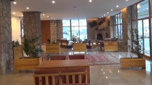 A spacious lobby with stone walls, large windows, and a fireplace. - Askireg Hotel (Pülümür)