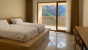 A hotel room with a large bed, a wooden desk, and a balcony with a mountain view. - Askireg Hotel (Pülümür)
