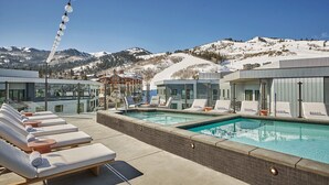 A poolside area with lounge chairs and a pool, surrounded by buildings with large windows, set against a snowy mountain backdrop. - Resort amenities high end luxury, Rooftop pool, Onsite spa and restaurants, Luxury 2BR Condo (Park City)
