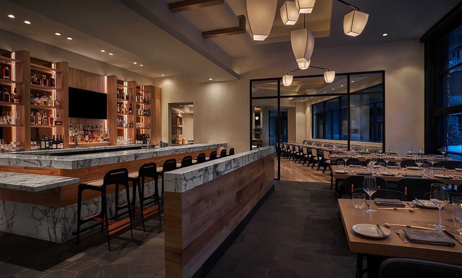 Un restaurant moderne doté d’un bar, de comptoirs en marbre et d’une longue table à manger dressée pour le repas.