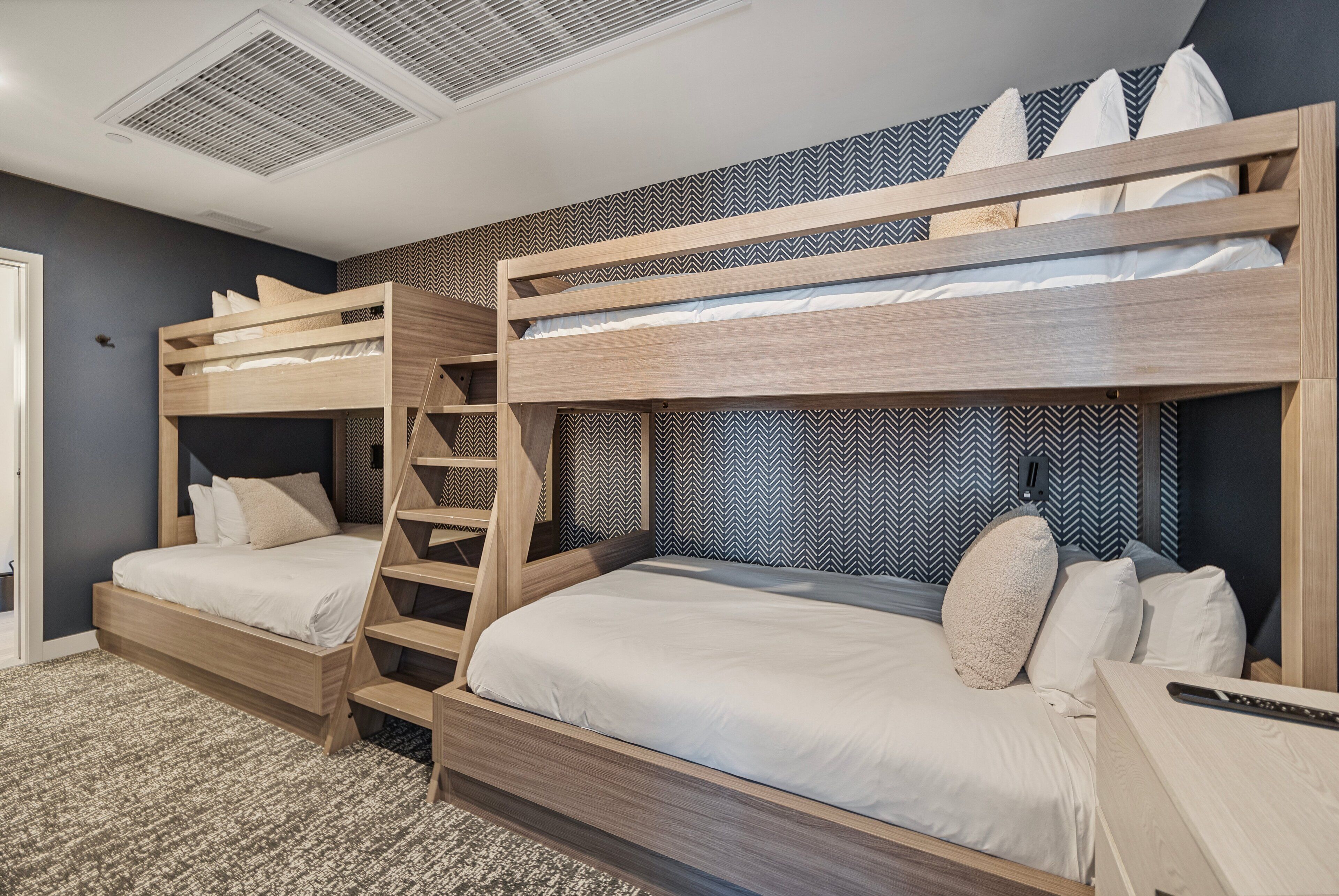 A bunk bed room with a herringbone-patterned wall, a wooden headboard, and a small bedside table.