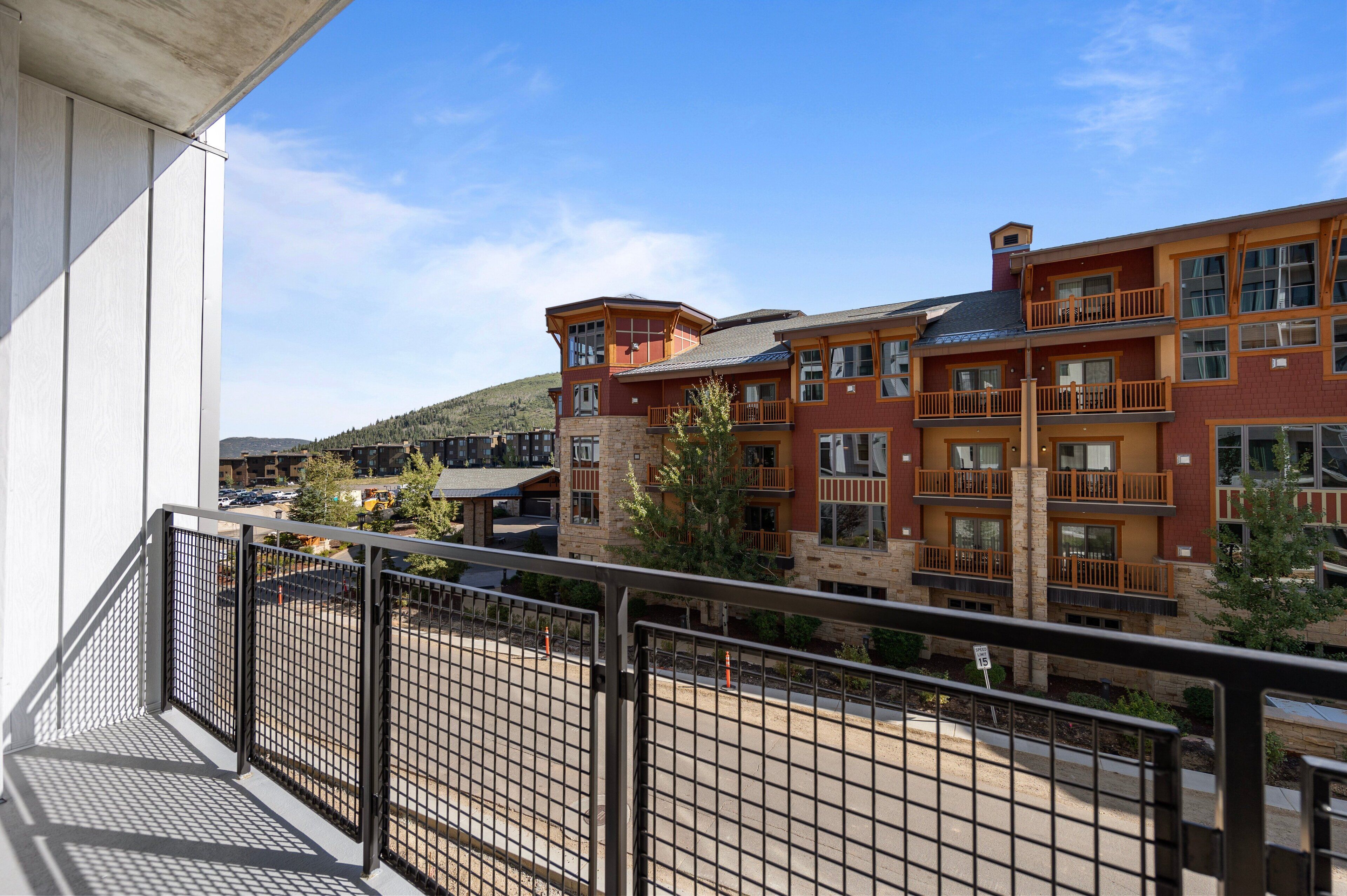 A multi-story hotel with balconies, a parking lot, and a view of a hilly landscape.
