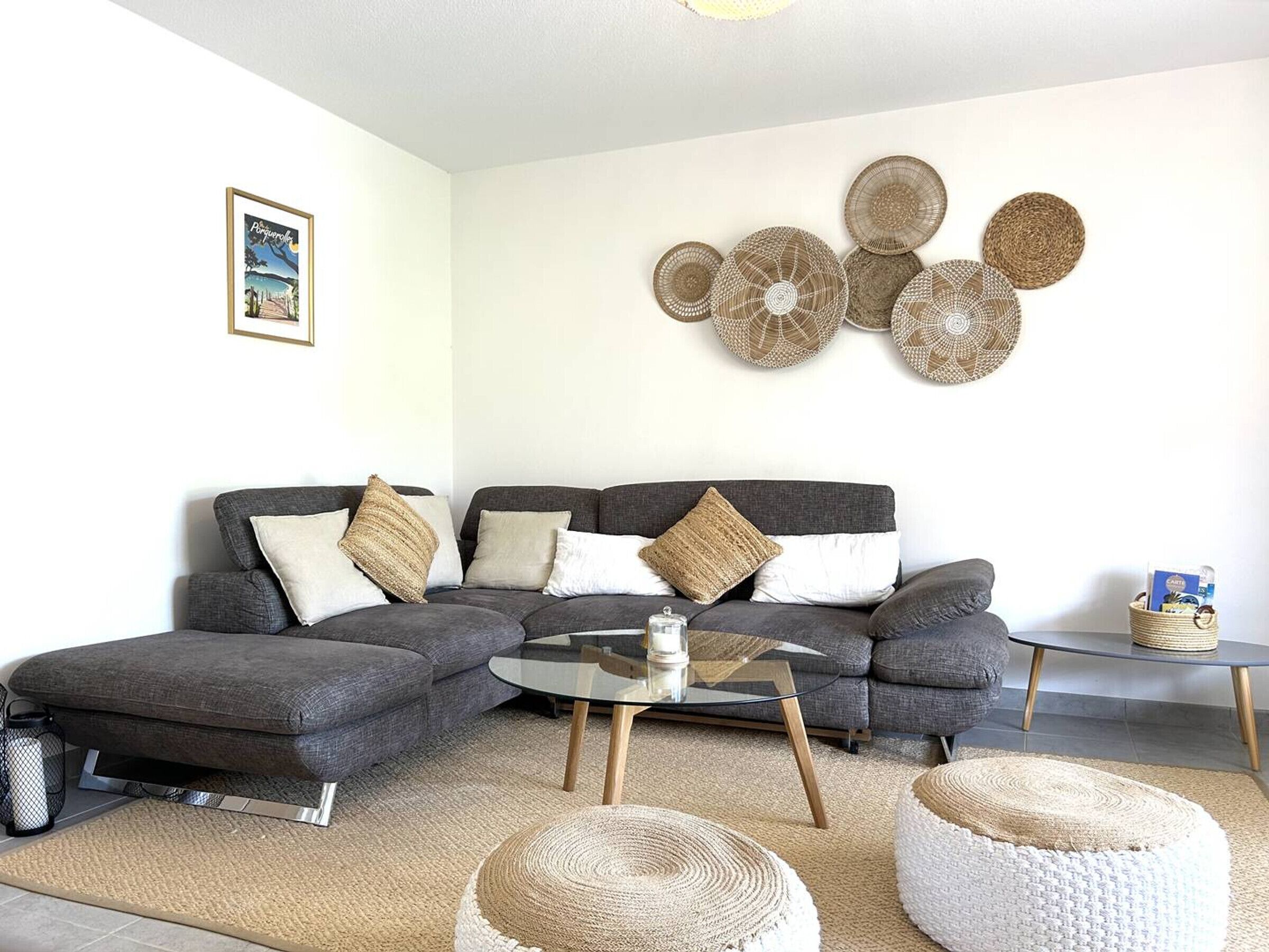 A modern living room with a grey sectional sofa, a glass coffee table, and woven poufs.