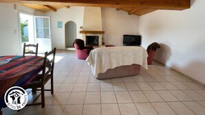 Une pièce spacieuse avec un haut plafond en bois, une cheminée, un téléviseur et un lit recouvert d’une couverture blanche.