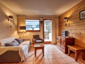 A cozy living room with a sofa, armchair, wooden cabinet, and a television.