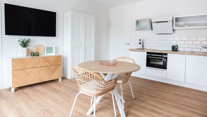 Eine moderne Küche mit weißen Schränken, einem Holztisch, Korbstühlen und einem Flachbildfernseher, der über der Arbeitsfläche angebracht ist.