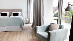 Ein modernes Schlafzimmer mit Bett, Sessel, Nachttisch und einem Fenster mit Vorhängen.