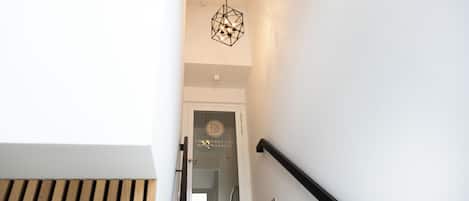 A staircase with a geometric pendant light, a wooden slatted wall, and a door with a logo.