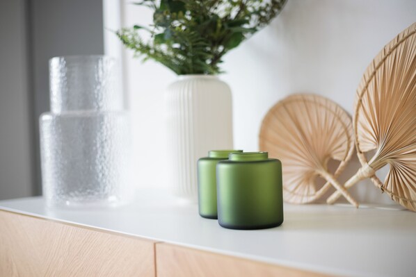 A white countertop with a clear glass, a white vase with green foliage, and two green cylindrical objects. - Bed & butter | Boardinghouse Hasbergen - Apartment No. 5 (Hasbergen)