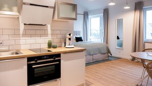A modern kitchen with a built-in oven, a coffee machine, and a small plant. There is a dining area with a round table and chairs.