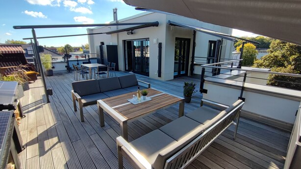 A rooftop terrace with a wooden deck, outdoor seating area, and a view of a modern building. - 3-room apartment (approx. 141 m²) for 6 people, with large roof terrace, in a quiet location (Graal-Müritz)