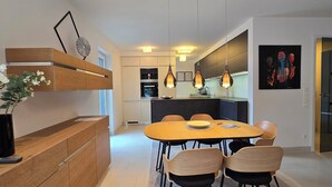 A modern dining area with a wooden table and chairs, a black vase with white flowers, and a kitchen in the background. - 3-room apartment (approx. 141 m²) for 6 people, with large roof terrace, in a quiet location (Graal-Müritz)