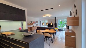 A modern kitchen with dark cabinetry, a central island, and a dining area with a round table and chairs. - 3-room apartment (approx. 141 m²) for 6 people, with large roof terrace, in a quiet location (Graal-Müritz)