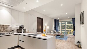 Uma cozinha moderna com uma ilha central, uma área de refeições com sofá e mesa de centro, e uma janela grande com vista para edifícios.