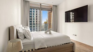 Quarto moderno com uma cama grande, uma televisão na parede e vista para a cidade através da janela.