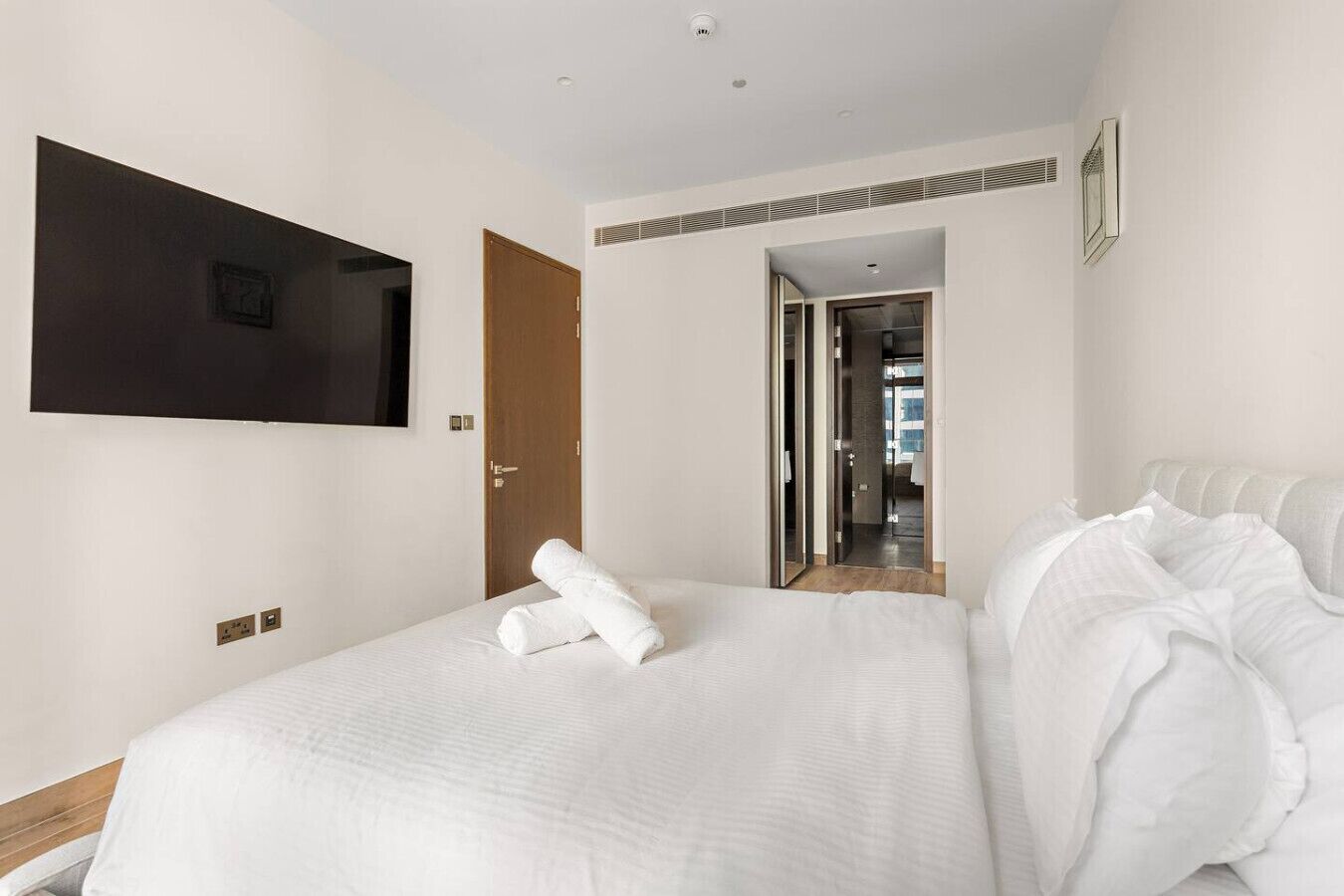 Ett hotellrum med en stor säng, en platt-TV som är monterad på väggen och en dörr som leder ut till en korridor.