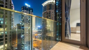 Um edifício alto com varanda de vidro que dá para a paisagem urbana à noite.