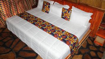 A bed with a patterned bedspread and pillows, a wooden headboard, and a stone-tiled floor.
