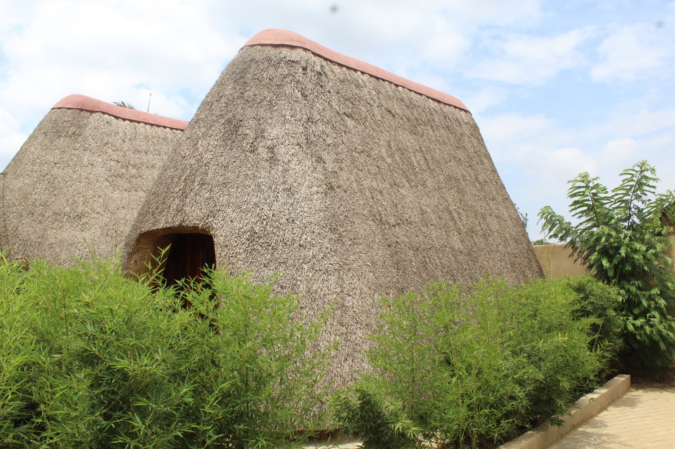 A traditional thatched-roof structure with a central doorway, surrounded by dense greenery.