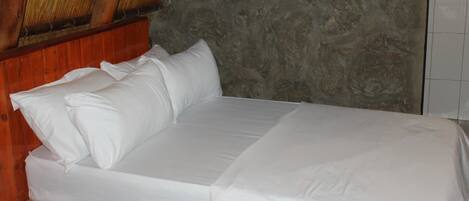 Una cama con ropa blanca en una habitación con pared de piedra y vigas de madera en el techo.