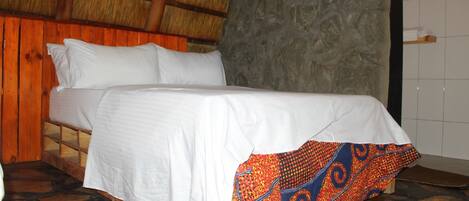 Un lit avec du linge de lit blanc et une couverture colorée à motifs, un mur en pierre et un plafond en bois.
