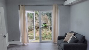 A spacious room with a grey couch, a door, and a view through a glass door to an outdoor area. - Victoria Avenue Charm - Manchester Hideaway (Manchester)
