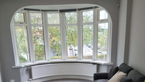 A modern living room with a curved window, a grey sofa, and a radiator under the window. - Victoria Avenue Charm - Manchester Hideaway (Manchester)