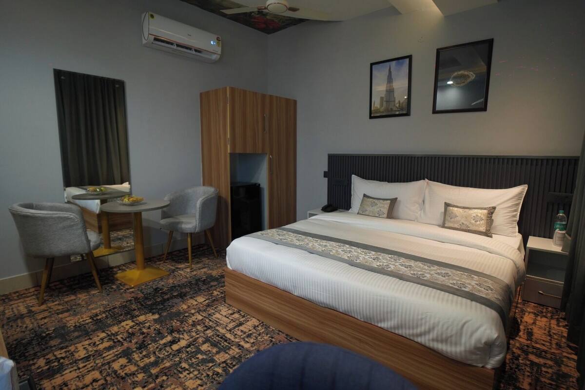 A hotel room with a bed, a desk with a chair, a wardrobe, and two framed pictures on the wall.