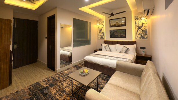 Une chambre d’hôtel moderne avec un lit, un canapé et une petite table. On y trouve un luminaire au plafond et un climatiseur fixé au mur.