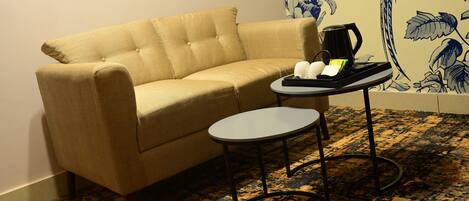 A beige sofa, a small round table with a tray, and a coffee maker on the floor.