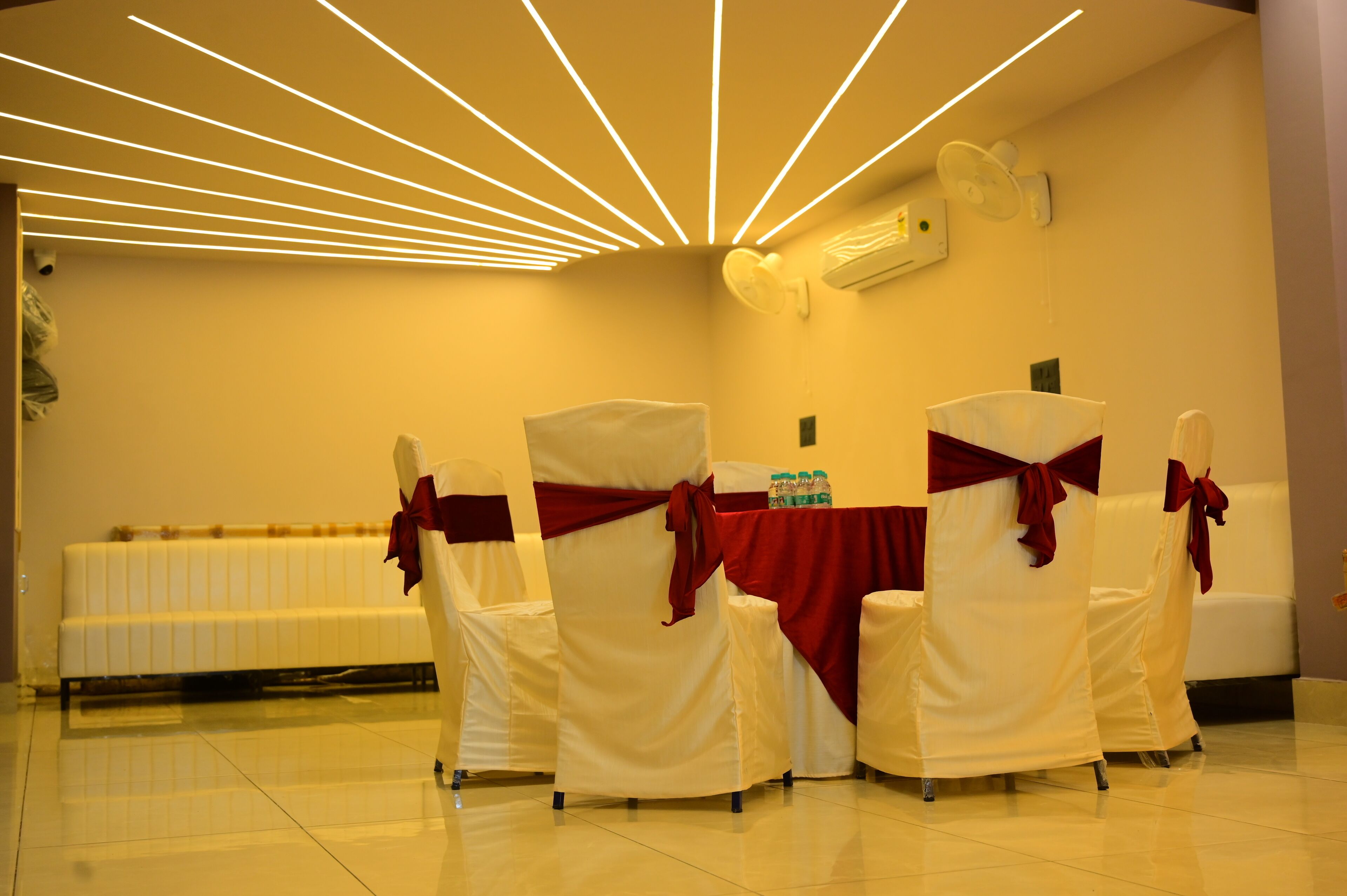 Un salón de conferencias con sillas y mesas blancas, lazos rojos y luces de techo.