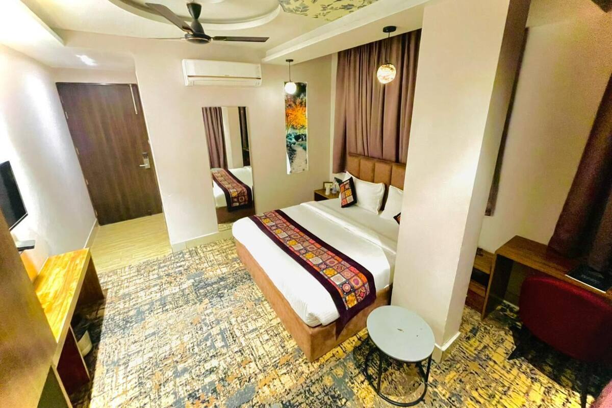 A hotel room with a bed, a small round table, a ceiling fan, and a wall-mounted air conditioner.