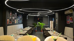 Un restaurant doté d’une longue table dressée pour le dîner, entourée de banquettes, et agrémenté de luminaires circulaires au design moderne.