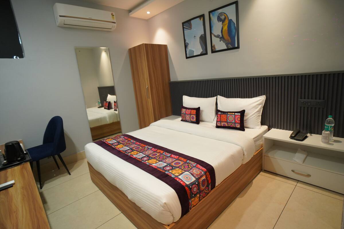 A hotel room with a bed, a desk, a chair, a nightstand, a mirror, and two wall art pieces.