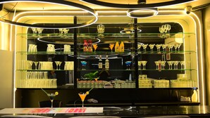Un espace bar doté de plusieurs étagères remplies de verres et de bouteilles, éclairé par des lampes rondes.