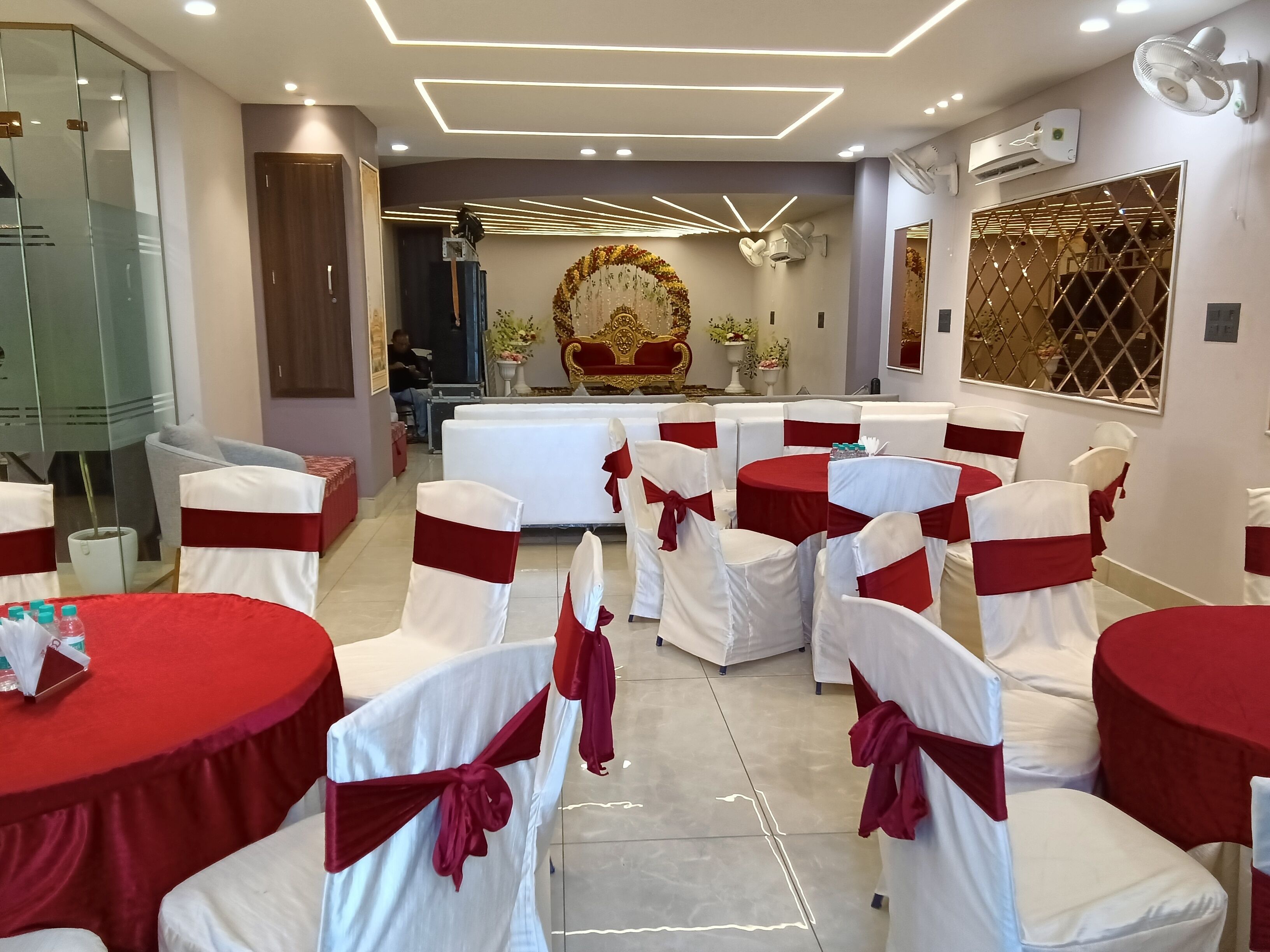 A conference room with white chairs and red tablecloths, a large ornate chair, and a decorative wall.