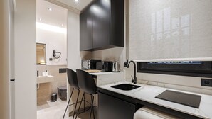 A modern kitchen with a black countertop, a built-in stove, and a sink. There are two black bar stools and a white refrigerator.