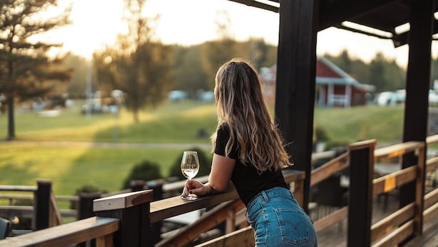 Una persona apoyada en una barandilla de madera, sosteniendo una copa de vino blanco, con vistas a un campo de golf.