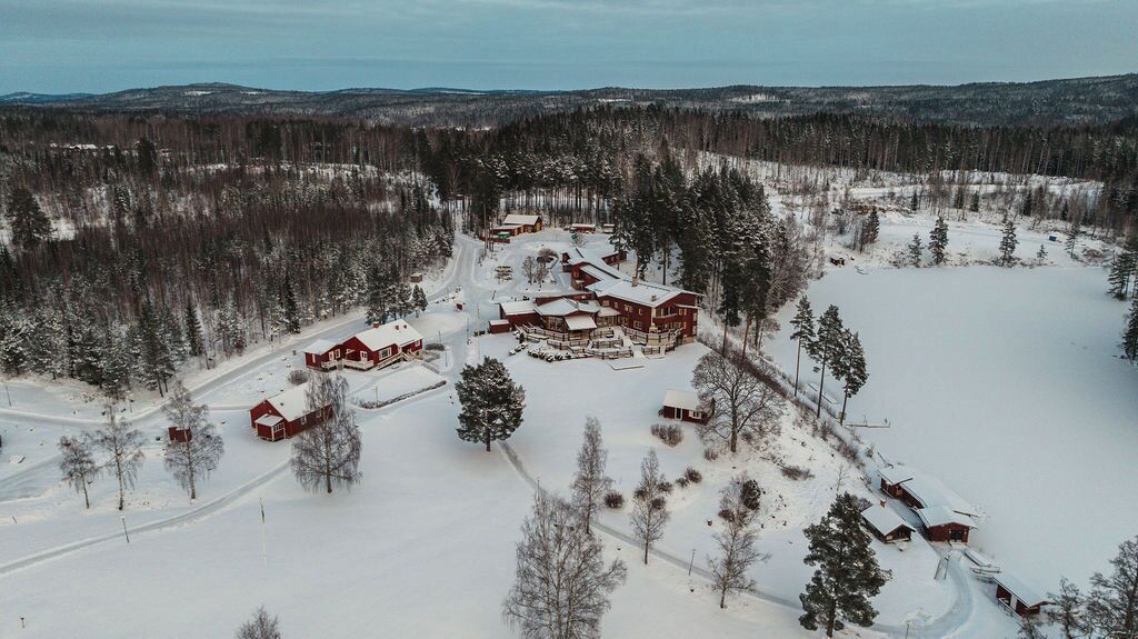 Un chalet enneigé composé de plusieurs bâtiments, entouré d’une forêt et surplombant un ciel dégagé.