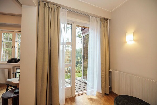 A room with a sliding glass door leading to an outdoor area, a small table with a chair, and a wall-mounted light fixture. - Barken Lodge (Smedjebacken)